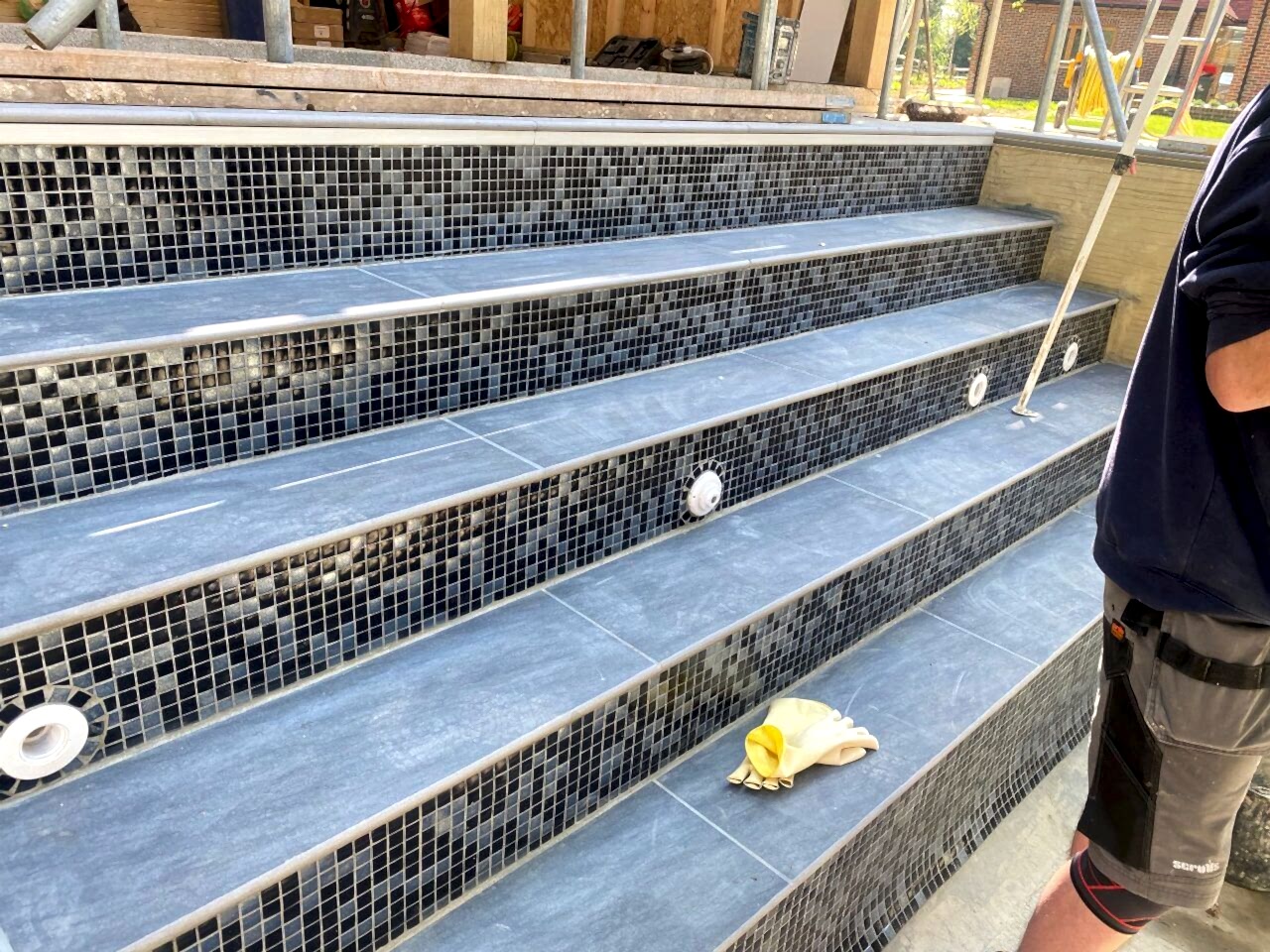 The steps also getting the same black and silver mosaic tiles like the swimming pool