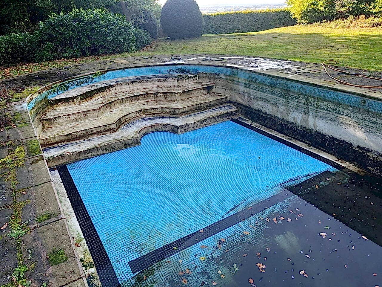 An existing frost damaged curved end concrete swimming pool prior to being refurbished