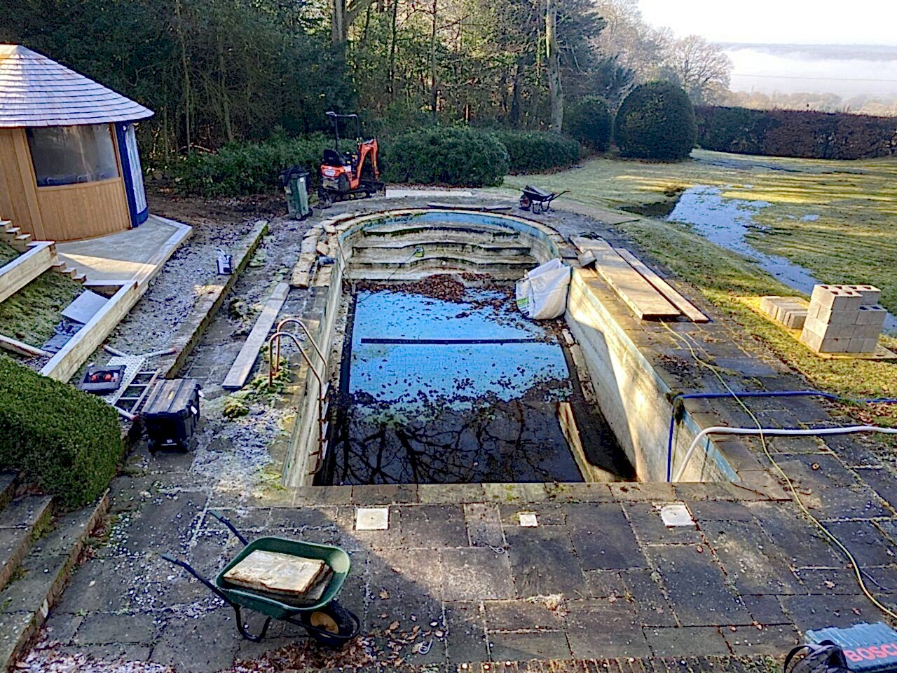 Existing swimming pool after water was removed showing frost damage, leaves and debris being removed