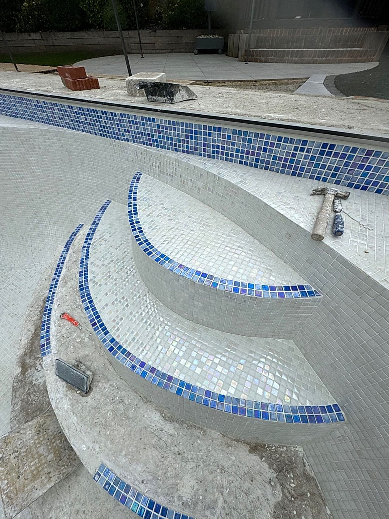 Close-up of the steps with the Ibiza 23.5mm iridescent glass mosaics and the sky blue tiles for the waterline